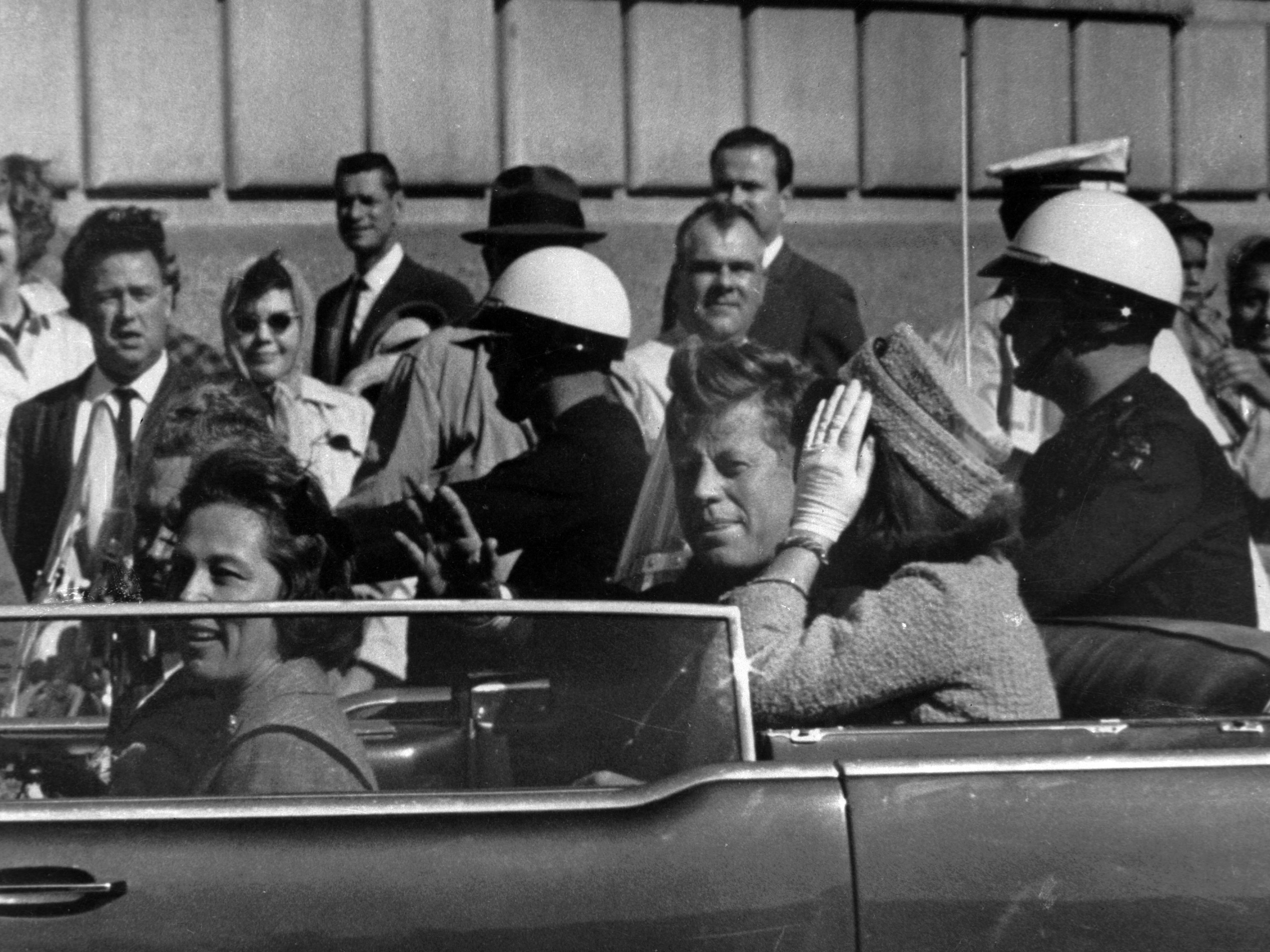 caption: President John F. Kennedy is seen riding in his motorcade approximately one minute before he was shot in Dallas on Nov. 22, 1963.