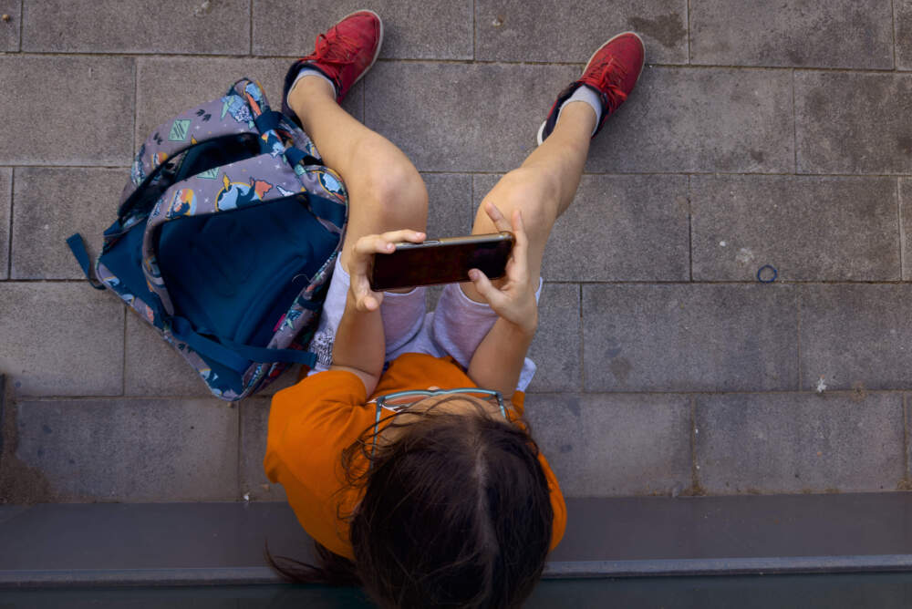 caption: A 11-year-old boy plays with his father's phone outside school in Barcelona, Spain, Monday, June 17, 2024. (Emilio Morenatti/AP)