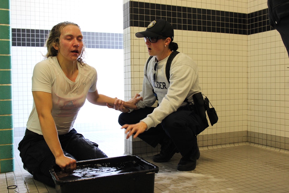 caption: Stephanie Schendel, 25, decided to become a police officer after reporting on crime and courts. The week before graduating from police academy, she was pepper-sprayed during training. Recruit Melissa Calder, a former Lamaze coach, helps her breathe.