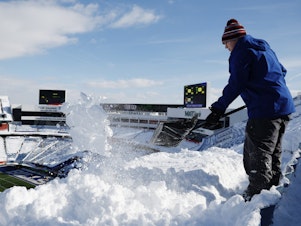 caption: Brady Reinagel shovels snow before the AFC Wild Card playoff game between the Buffalo Bills and Pittsburgh Steelers at Highmark Stadium in Buffalo, N.Y. The Bills hired local residents to help clear snow from the stadium before Monday's game.