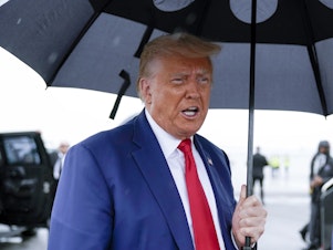caption: Former President Donald Trump speaks before he boards his plane at Ronald Reagan Washington National Airport on August 3 in Arlington, Va.