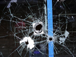 caption: Bullet holes from a prior shooting are still visible in a storefront window at the scene of a fatal overnight shooting on South Street in Philadelphia on June 5, 2022.