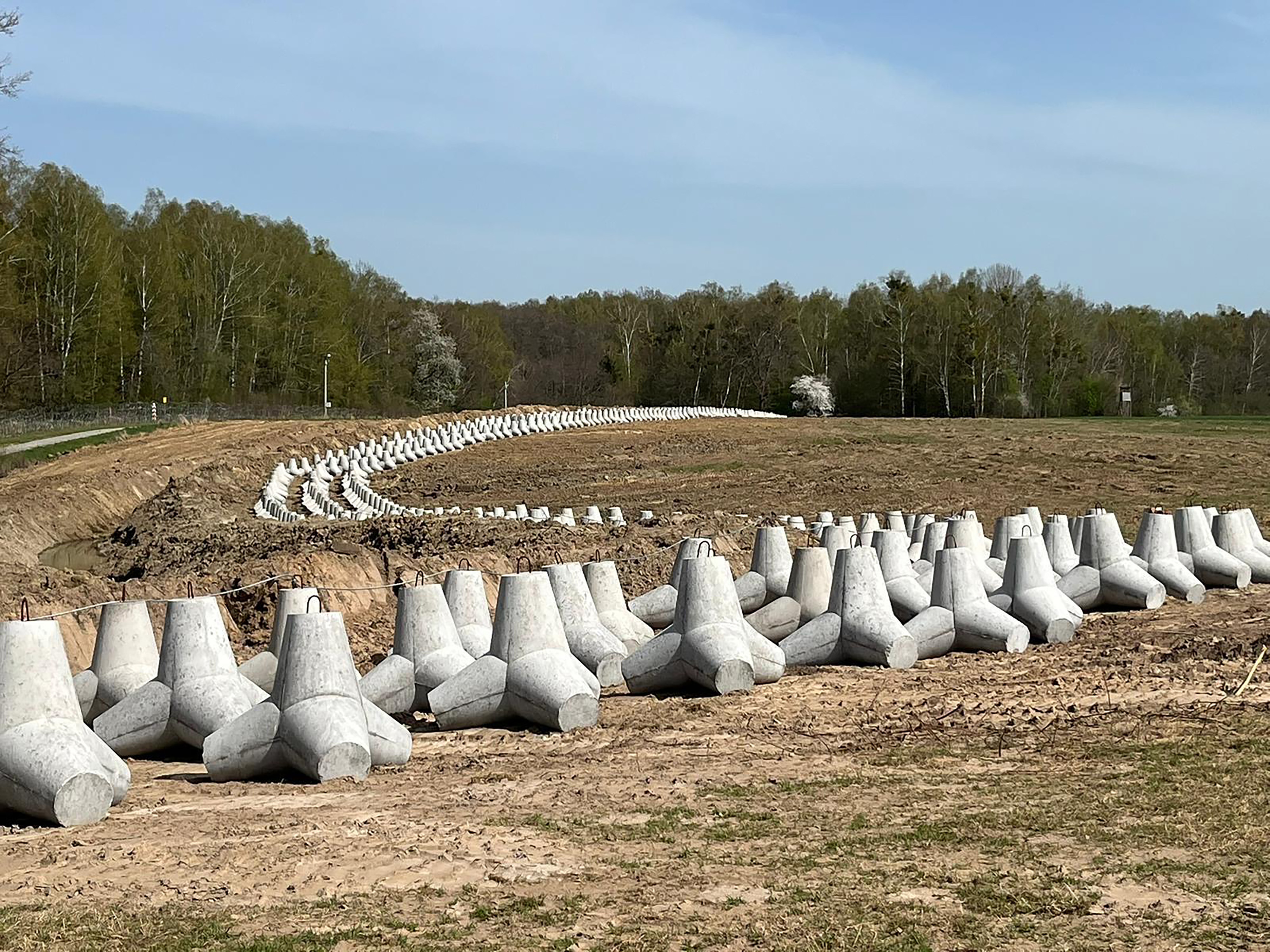 caption: Rows of concrete anti-tank structures called hedgehogs sit in a field along Poland's border with Russia.