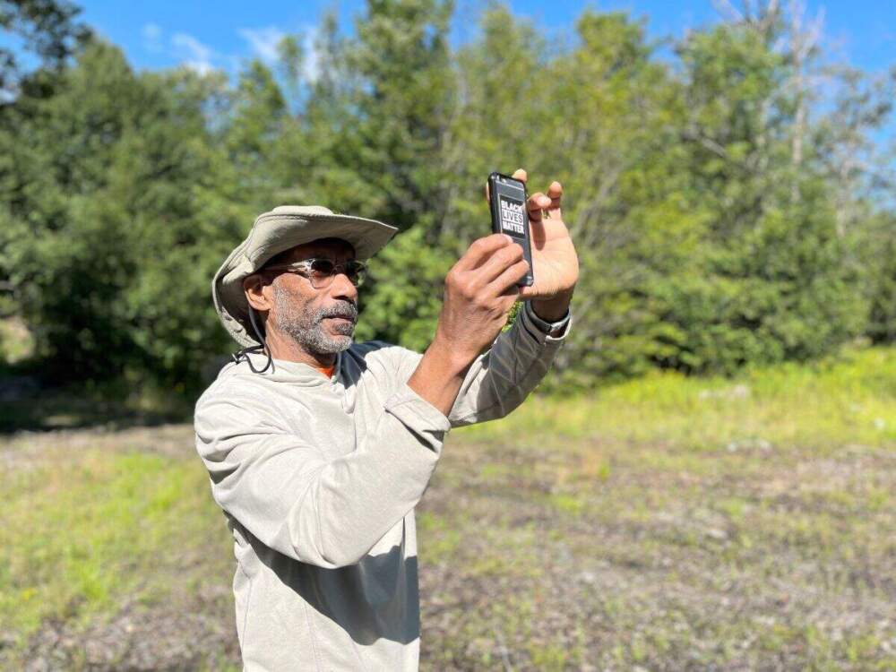 caption: Artist Keith Morris Washington takes photos of the general location in the central Adirondacks where a Black man was killed by a group of white men in March 1932. (Emily Russell/North Country Public Radio)