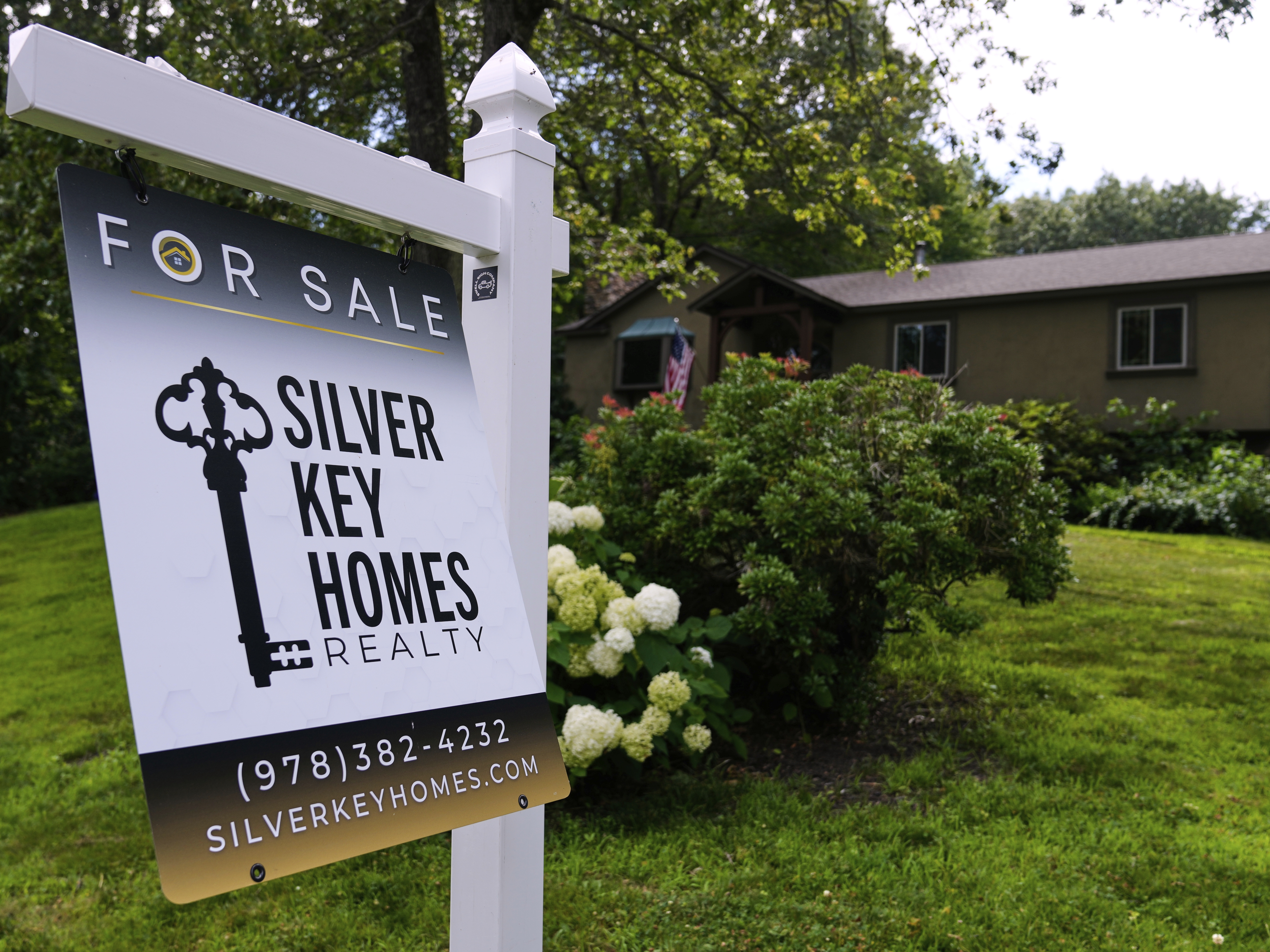 caption: A for sale sign is displayed in front of a single family home, on July 17, 2025, in Derry, N.H.