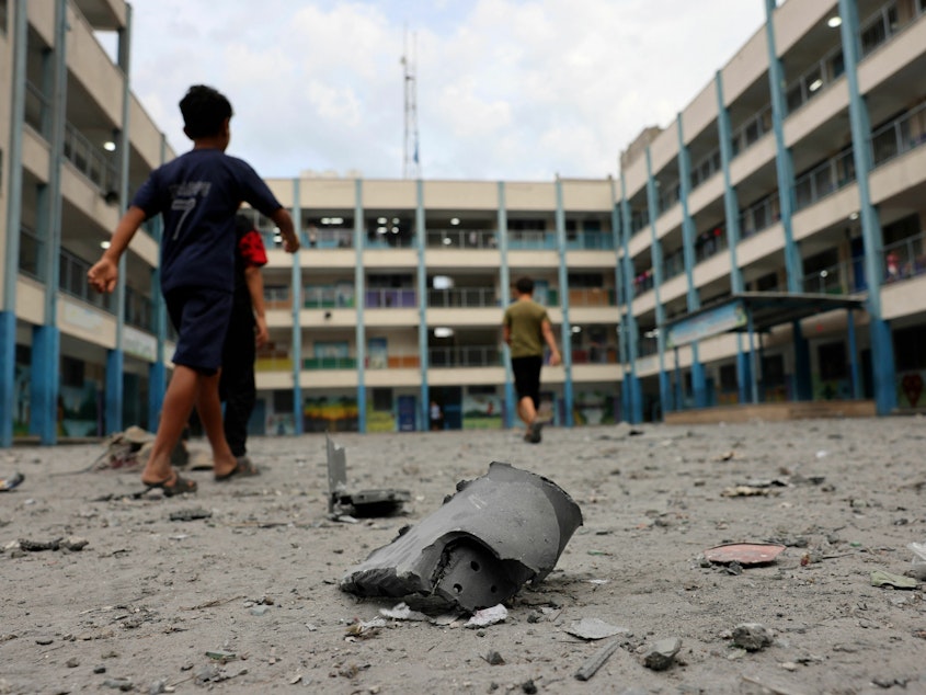caption: Palestinian children walk past debris in the courtyard of a school run by the United Nations Relief and Works Agency for Palestine refugees following Israeli airstrikes targeting Gaza City on Monday.