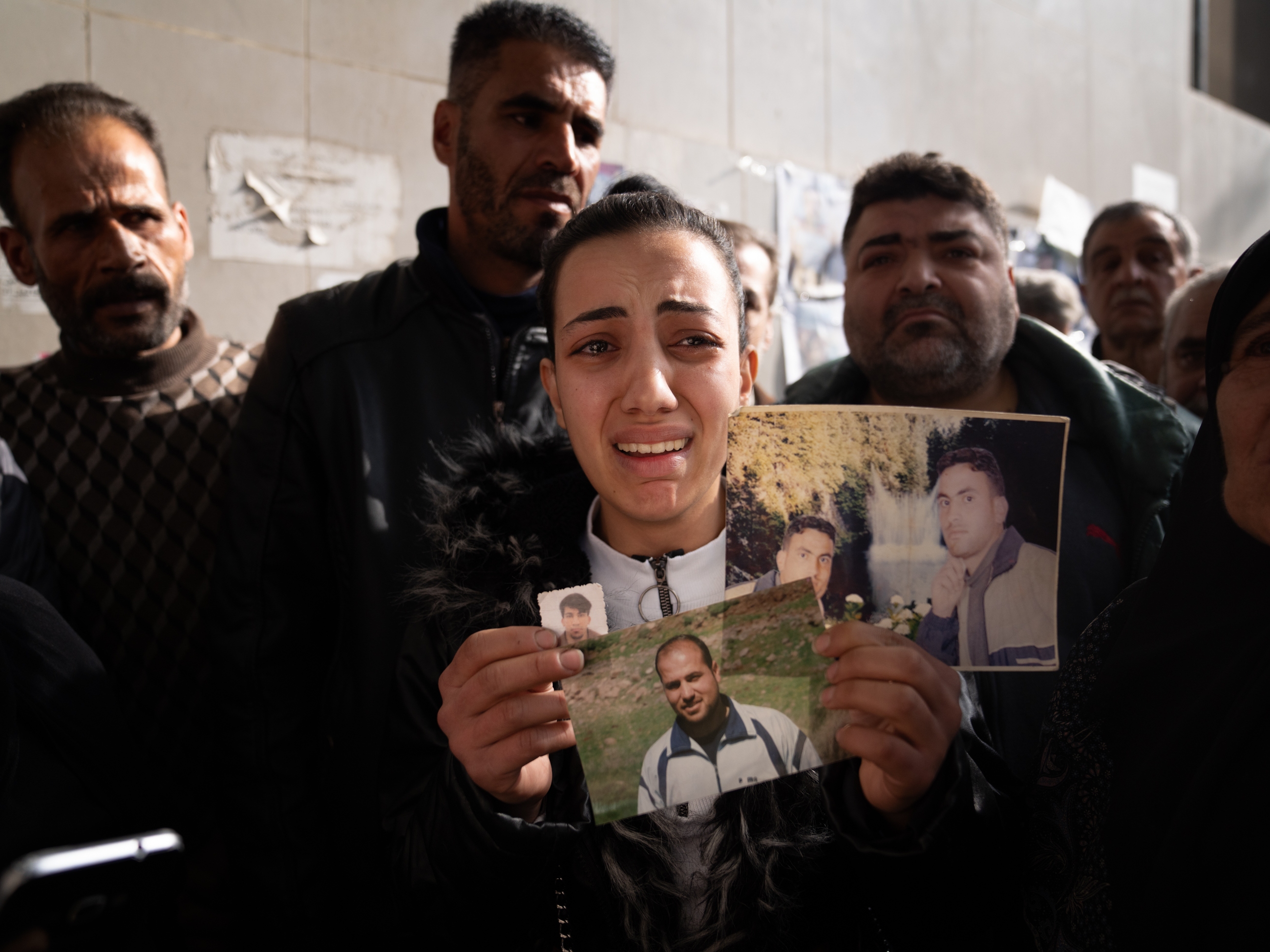 caption: Sarah Abdel Hamid Al-A'ami holds photos of her 4 brothers who were all accused of terrorism under the Assad regime, and though she came to search posters of dead bodies, she still hasn't found any signs of them.