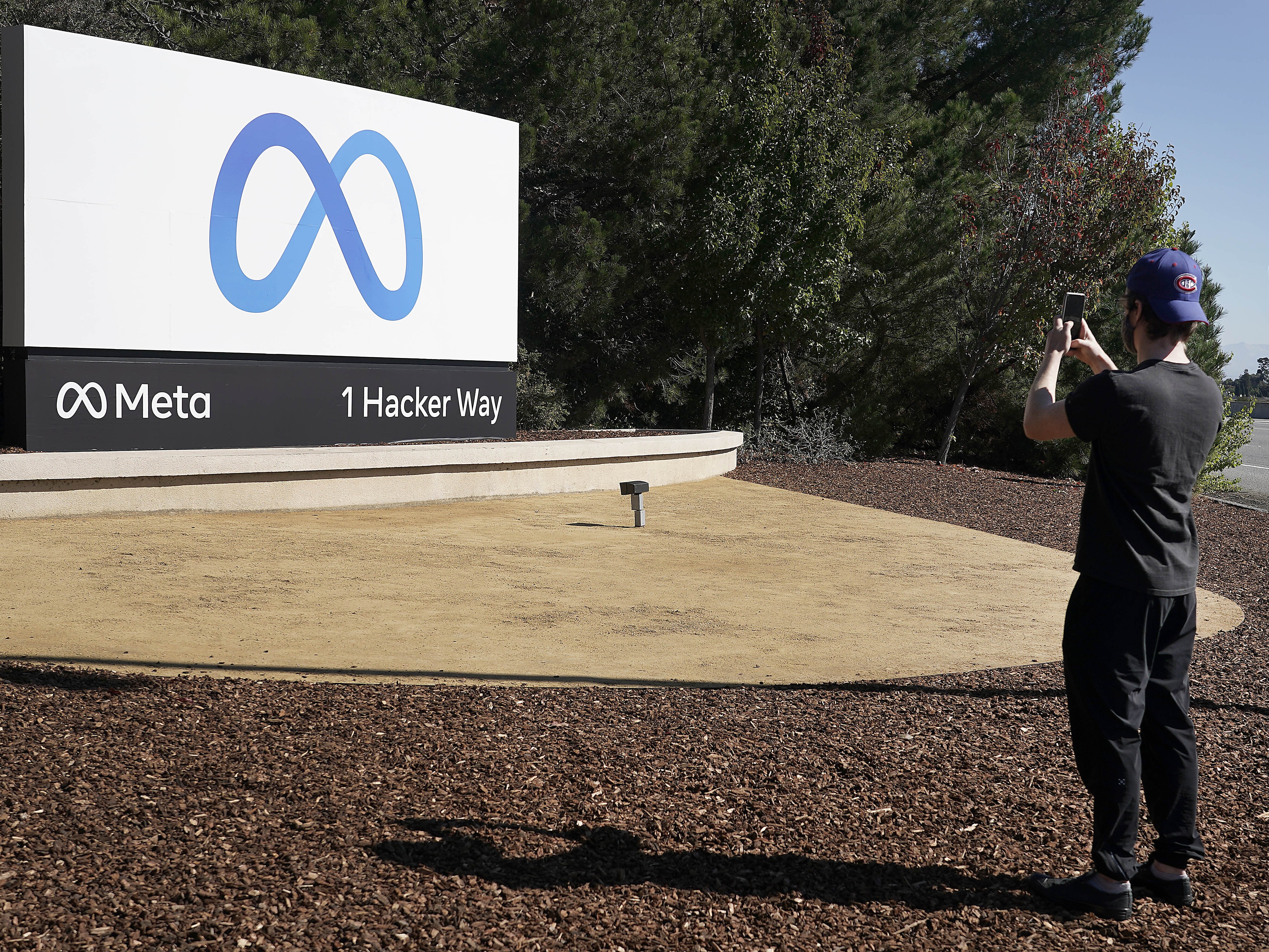 caption: Facebook employee take a photo in front of new Meta Platforms Inc. sign outside the company headquarters in Menlo Park, Calif., Thursday, Oct. 28, 2021.