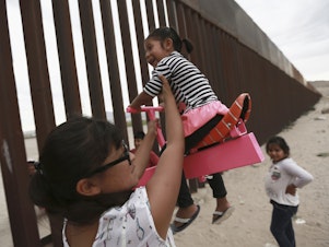 caption: A set of pink seesaws allowed people to share some fun along the U.S.-Mexico border wall this week. Here, a woman helps her little girls ride the seesaw that was installed near Ciudad de Juarez, Mexico.