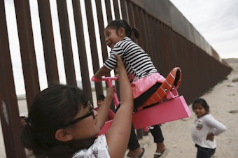 caption: A set of pink seesaws allowed people to share some fun along the U.S.-Mexico border wall this week. Here, a woman helps her little girls ride the seesaw that was installed near Ciudad de Juarez, Mexico.