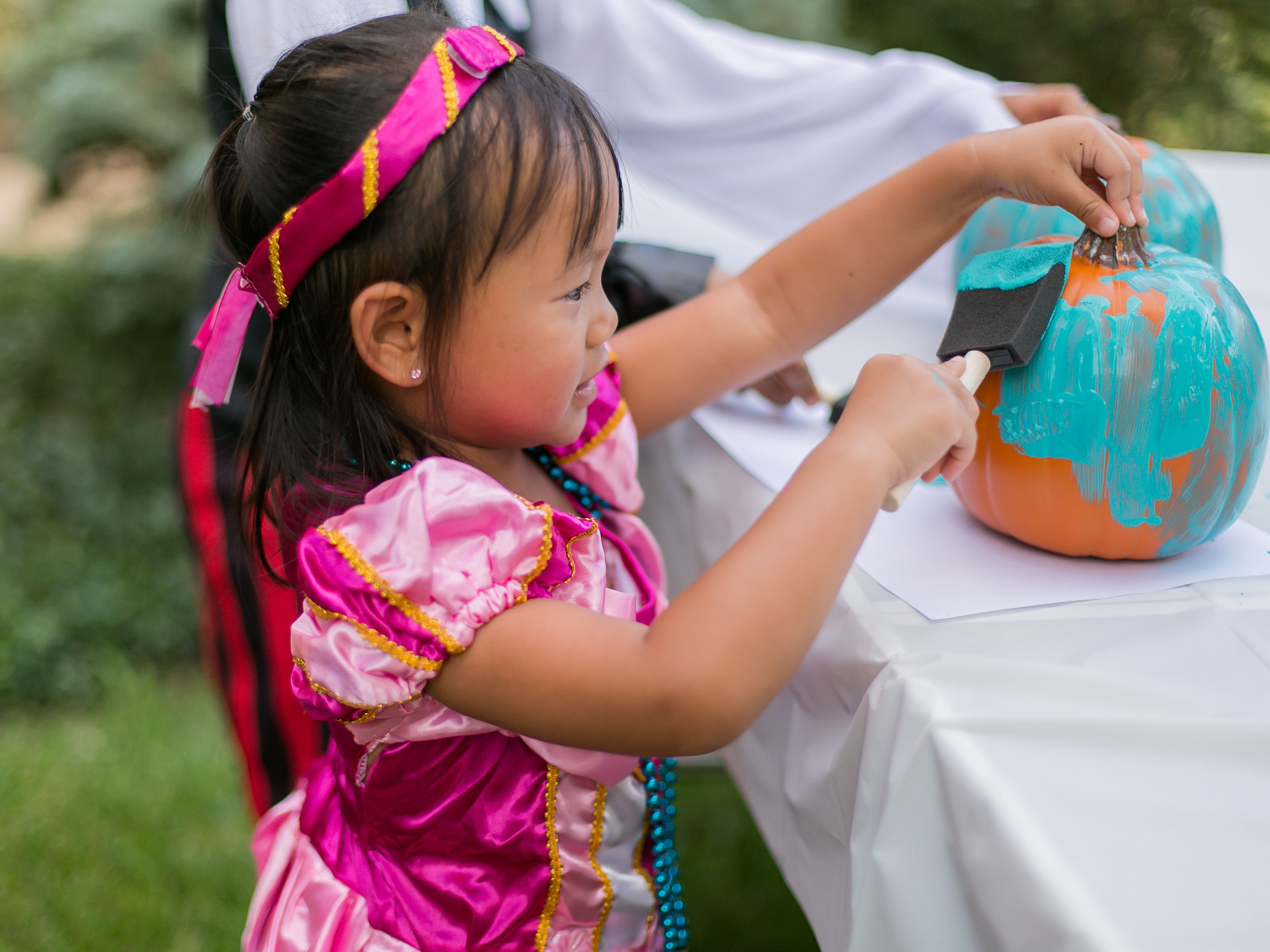 caption: A young girl paints a pumpkin teal to signify that a place is safe for children with food allergies to go trick-or-treating.