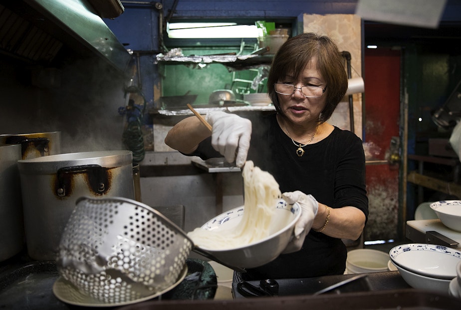 caption: Minh Pham portions out noodles for customers in 2017, in the kitchen at Pho Bac on S. Jackson St., in Seattle. 