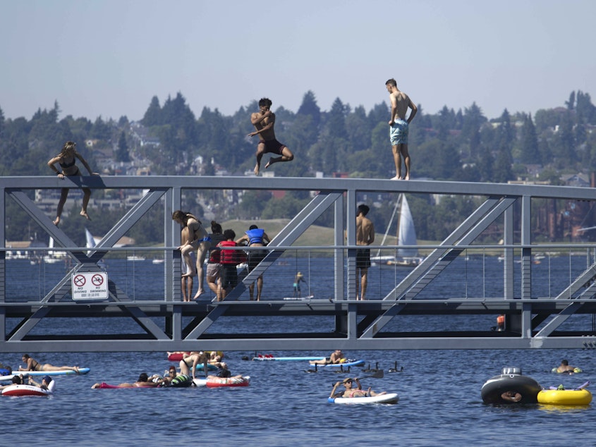 caption: People jump from a pedestrian bridge at Lake Union Park in Seattle as a record-setting heat wave blasts the Pacific Northwest.