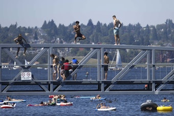 caption: People jump from a pedestrian bridge at Lake Union Park in Seattle as a record-setting heat wave blasts the Pacific Northwest.