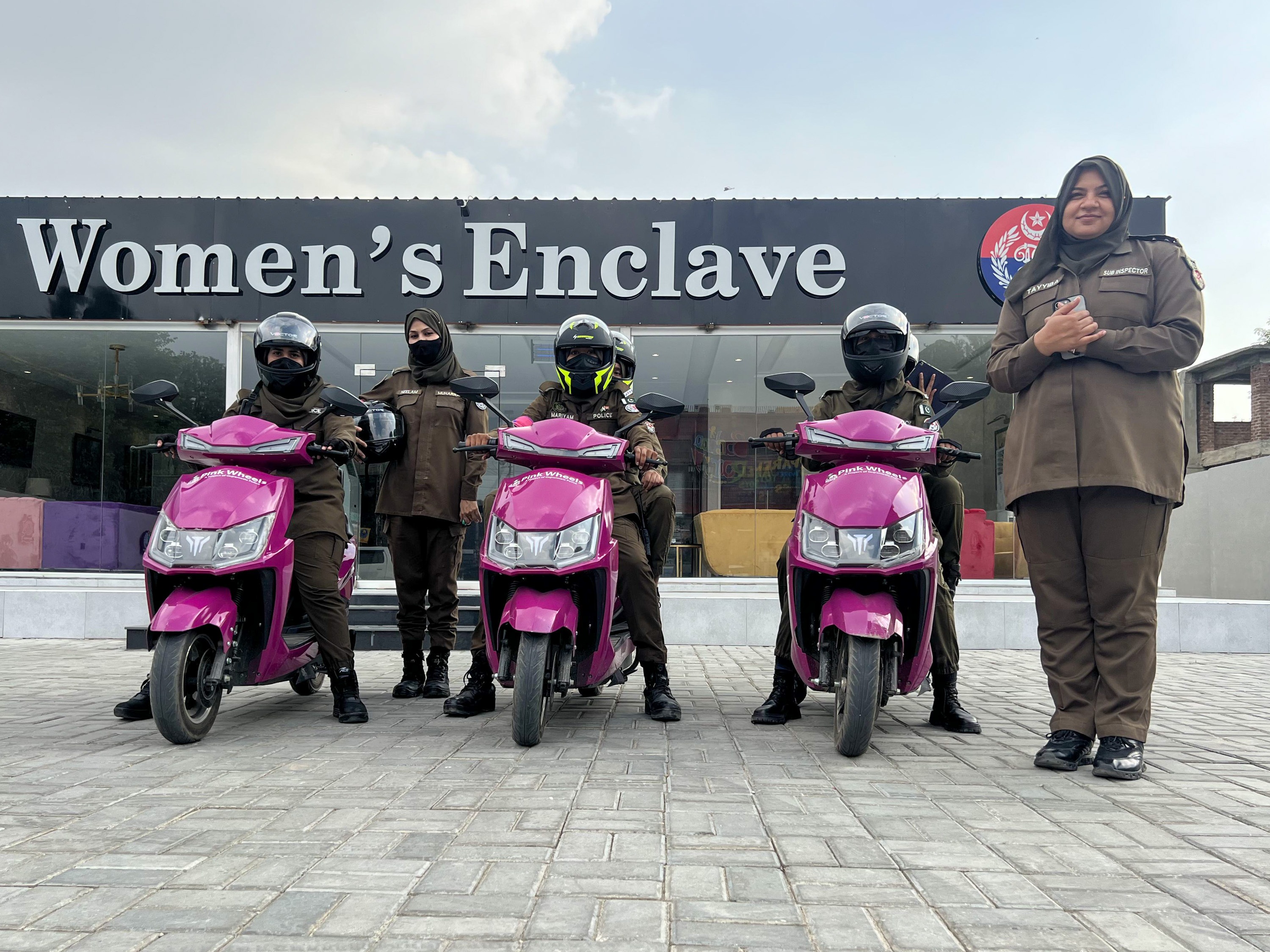 caption: The "Pink Wheels" team in the Pakistani town of Gujranwala consists of female officers who ride pink scooters to respond to complaints from women about domestic violence and sexual assault. The officers stand in front of the "Women's Enclave," a new kind of police station, staffed by women and intended for women who want to file such complaints. At right is Tayyiba Hameed, 32, who is on the staff of the Women's Enclave.