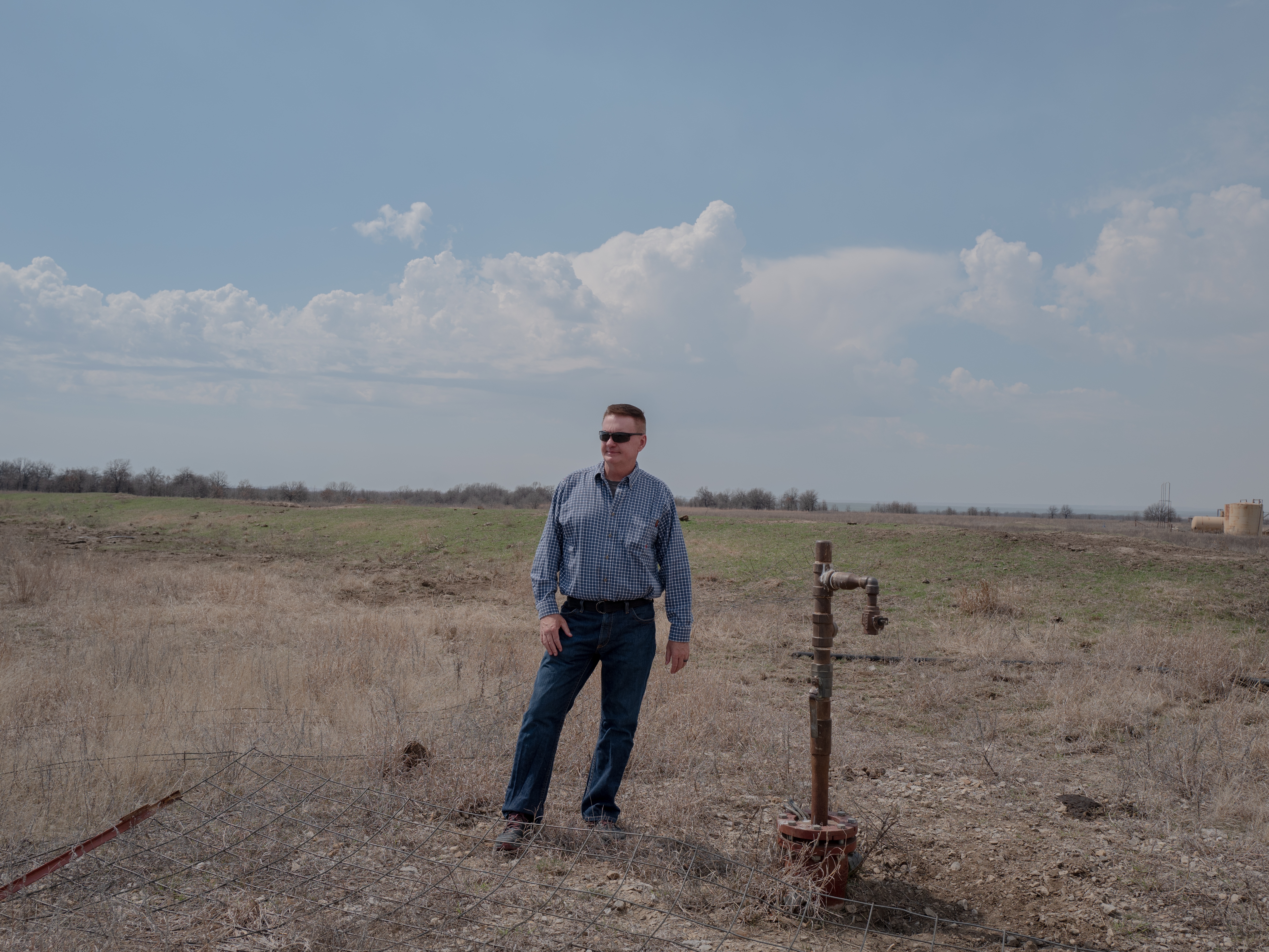 caption: Dan Arthur, the president and chief engineer of ALL Consulting, stands beside a defunct oil well in the Tallgrass Prairie Preserve in Oklahoma on March 20, 2024. The well has not been used for years — there's no pump attached to it. But it hasn't been properly plugged, either.