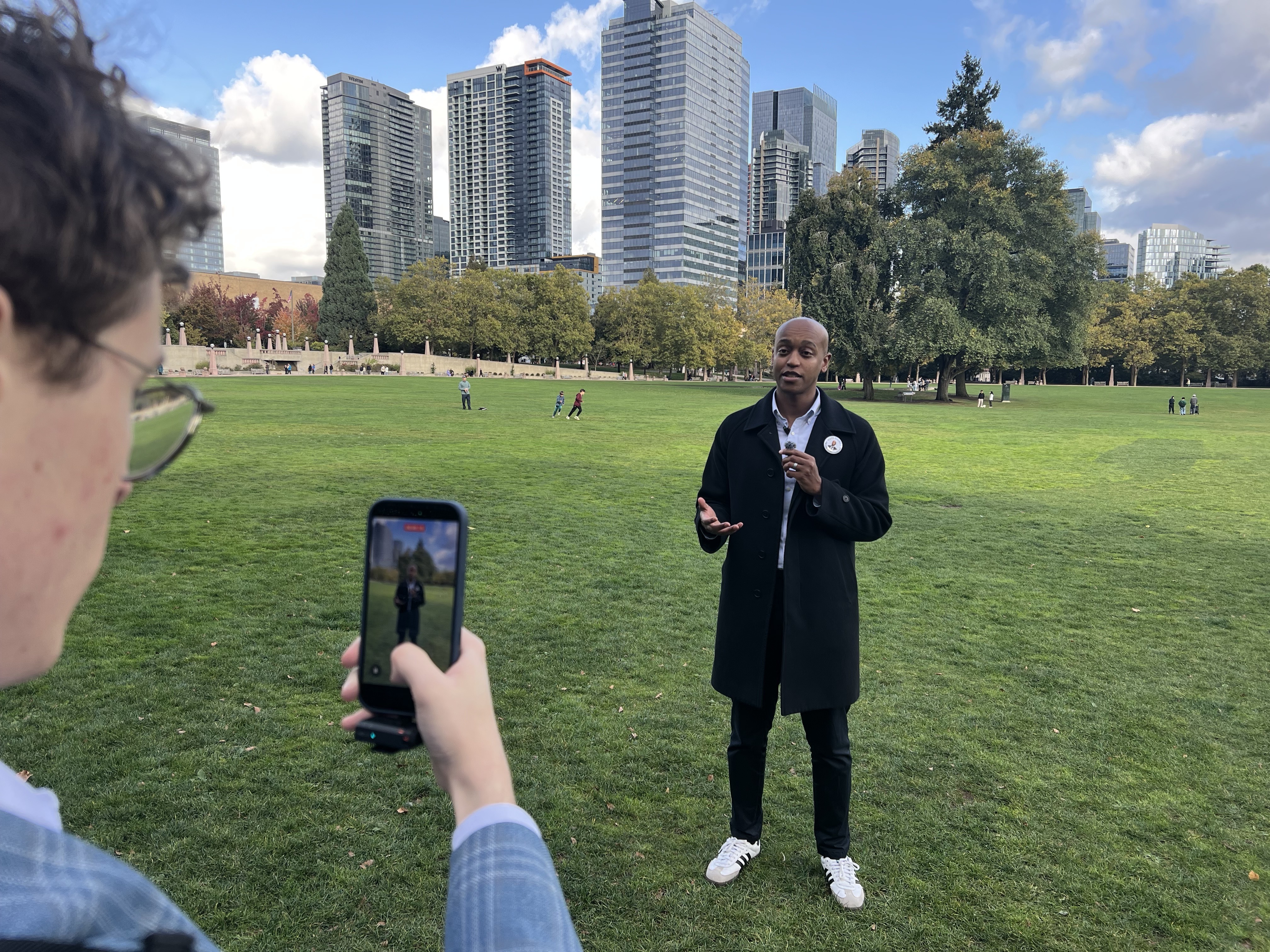 caption: King County Councilmember Girmay Zahilay, right, records a video for social media at Bellevue Downtown Park.