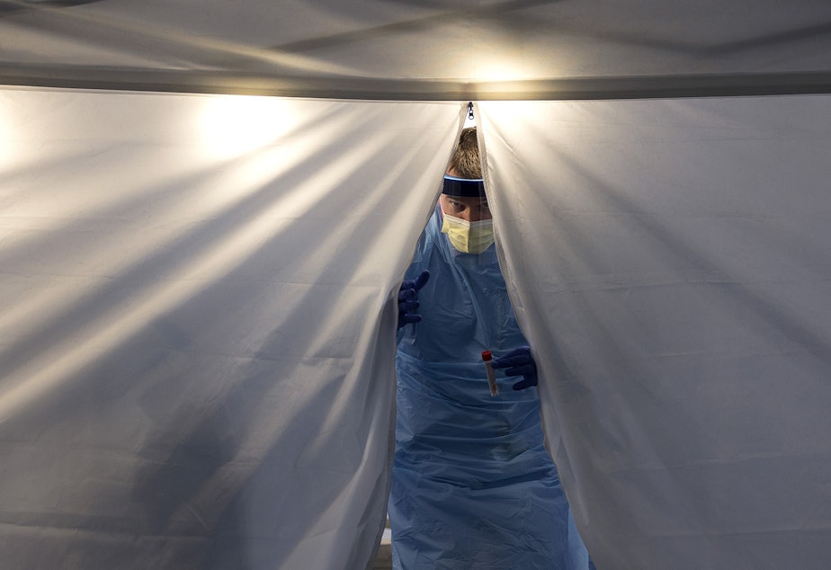 caption: Employee Health Nurse at UW Northwest Hospital Jeff Gates exits a tent at UW Medicine's drive-through coronavirus testing clinic on Thursday, March 12, 2020, in Seattle.