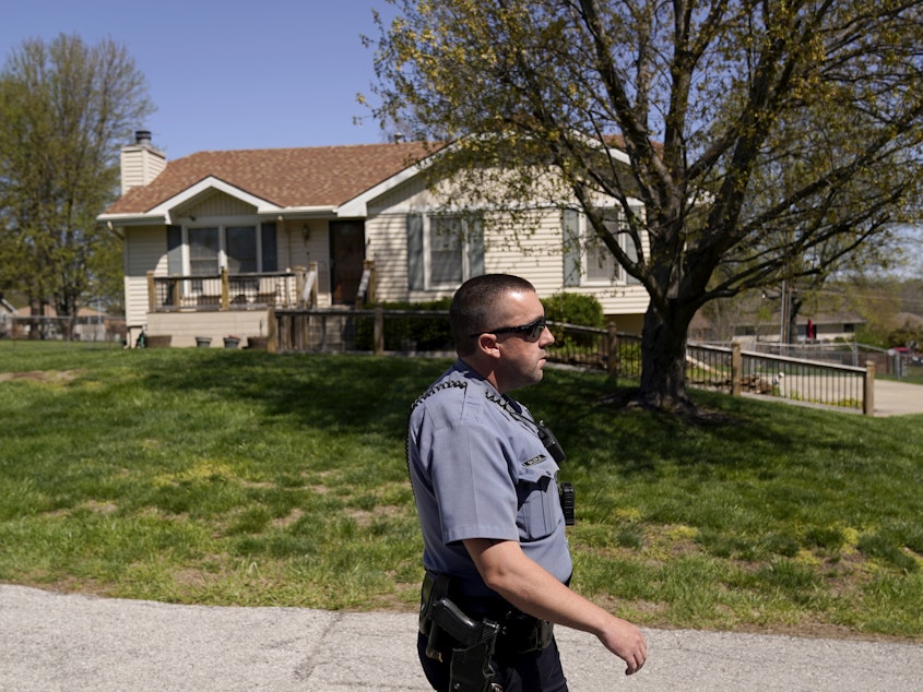 caption: A police officer walks past the house where a 16-year-old Black high school student was shot last week after his family says he went to the wrong address to pick up his younger siblings.