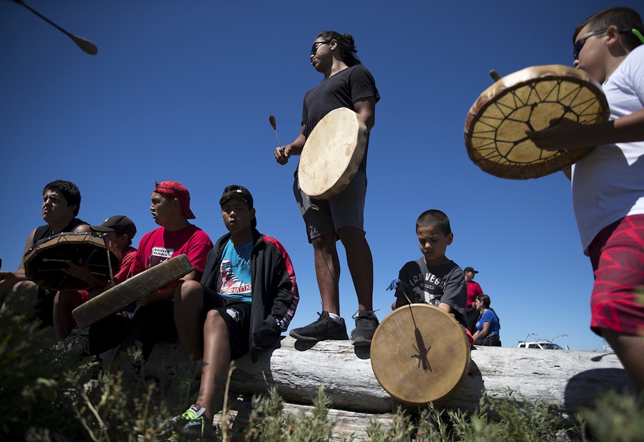 caption: ShxwhÃ¡:y drummer Leonard Gladstone, 17, center, drums on Thursday, July 27, 2017, while waiting for the 'Emma canoe' to arrive in Tsawassen, British Columbia.