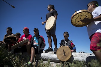 caption: ShxwhÃ¡:y drummer Leonard Gladstone, 17, center, drums on Thursday, July 27, 2017, while waiting for the 'Emma canoe' to arrive in Tsawassen, British Columbia.