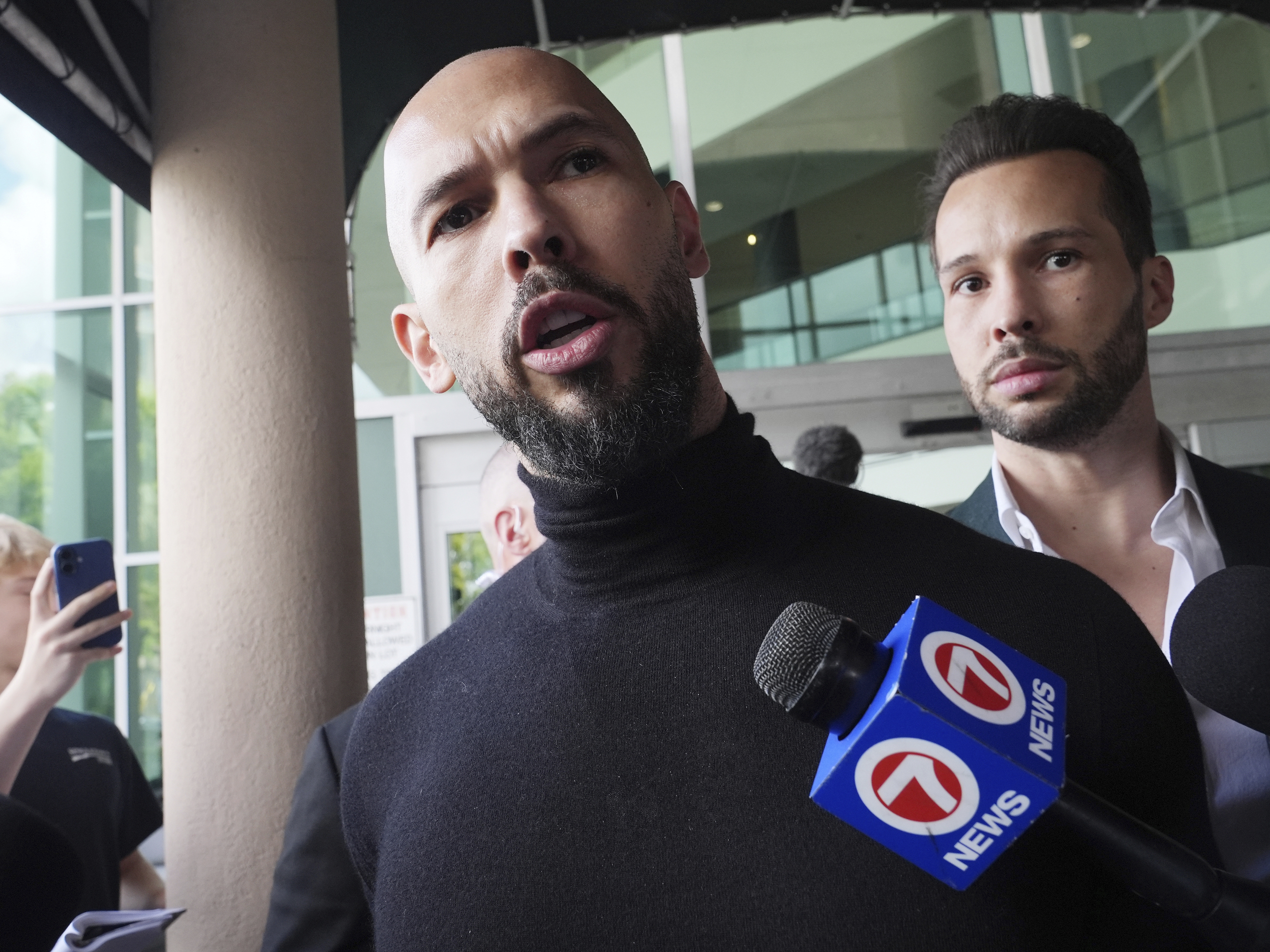 caption: Andrew Tate (foreground) and his brother Tristan arrive in Fort Lauderdale, Fla., on Thursday, after Romanian authorities lifted travel restrictions against them.