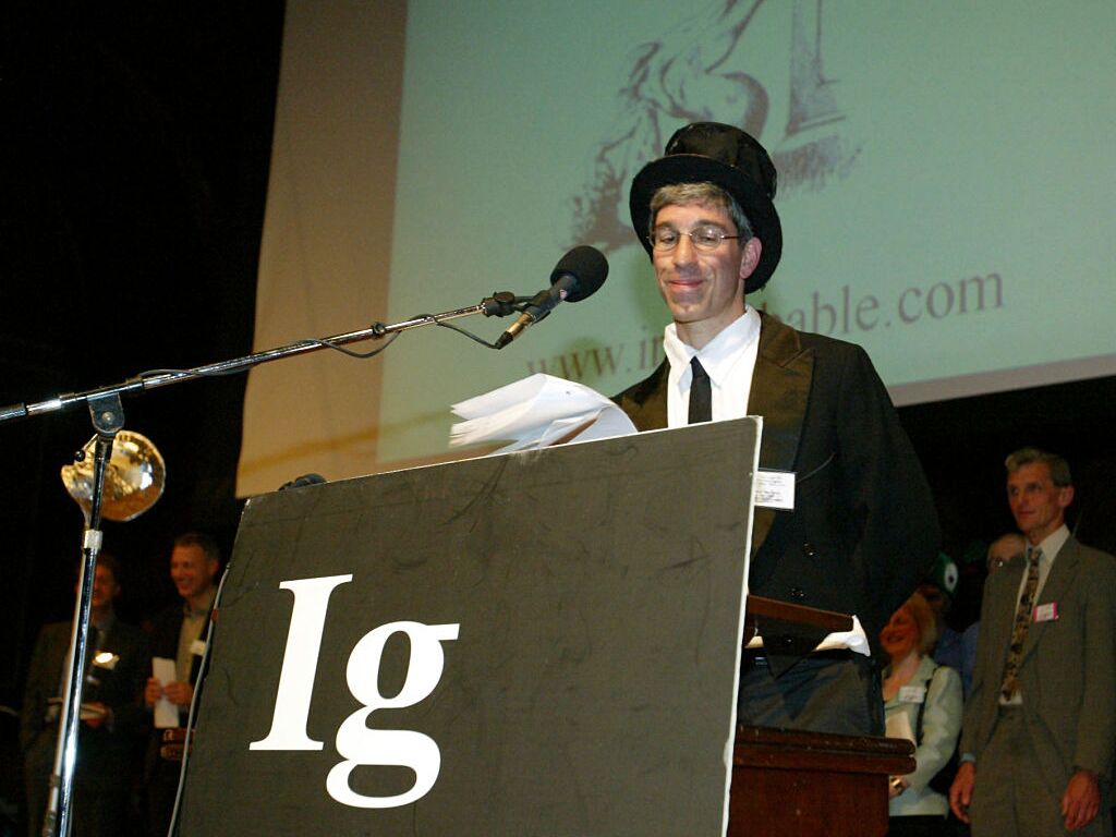 caption: Master of Ceremonies Marc Abrahams addresses the audience during a pre-pandemic Ig Nobel Prize ceremony.