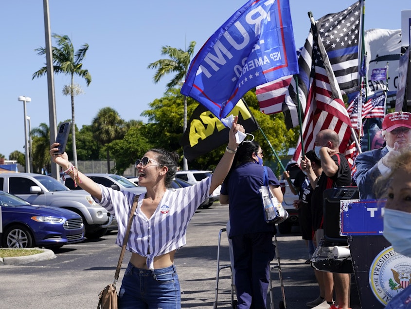 caption: Juliet Roa takes a selfie as supporters of President Donald Trump wave flags outside of an early voting location at the John F. Kennedy Library, Tuesday, Oct. 27, 2020, in Hialeah, Fla. (AP Photo/Lynne Sladky)