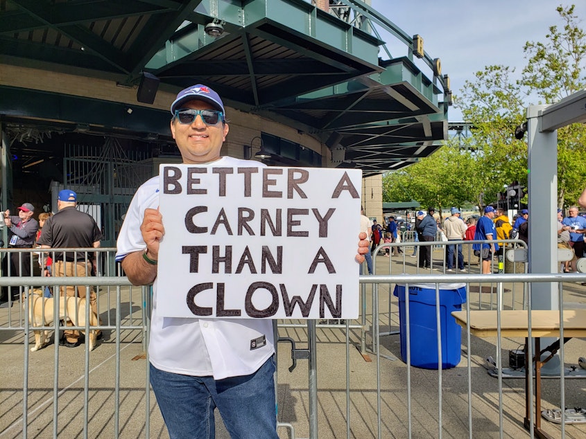 caption: A Toronto Blue Jays fan waives a sign that reads, "Better A Carney Than A Clown" in Seattle on Friday, May 9, 2025.