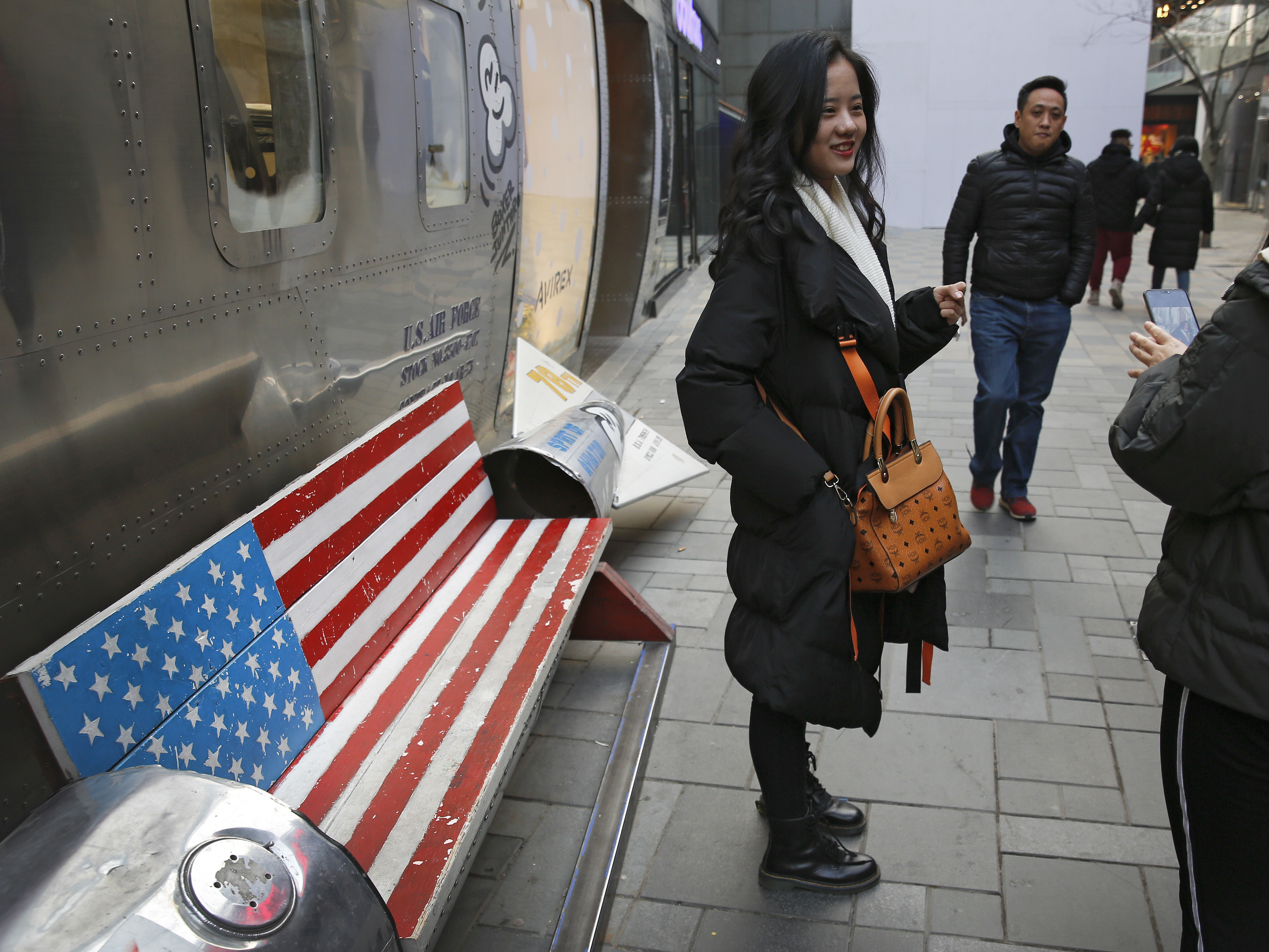 caption: Chinese shoppers spend their time next to a bench painted with the U.S. flag at the capital city's popular shopping mall in Beijing. During trade talks this week, the two sides face potentially lengthy wrangling over technology and the future of their economic relationship.