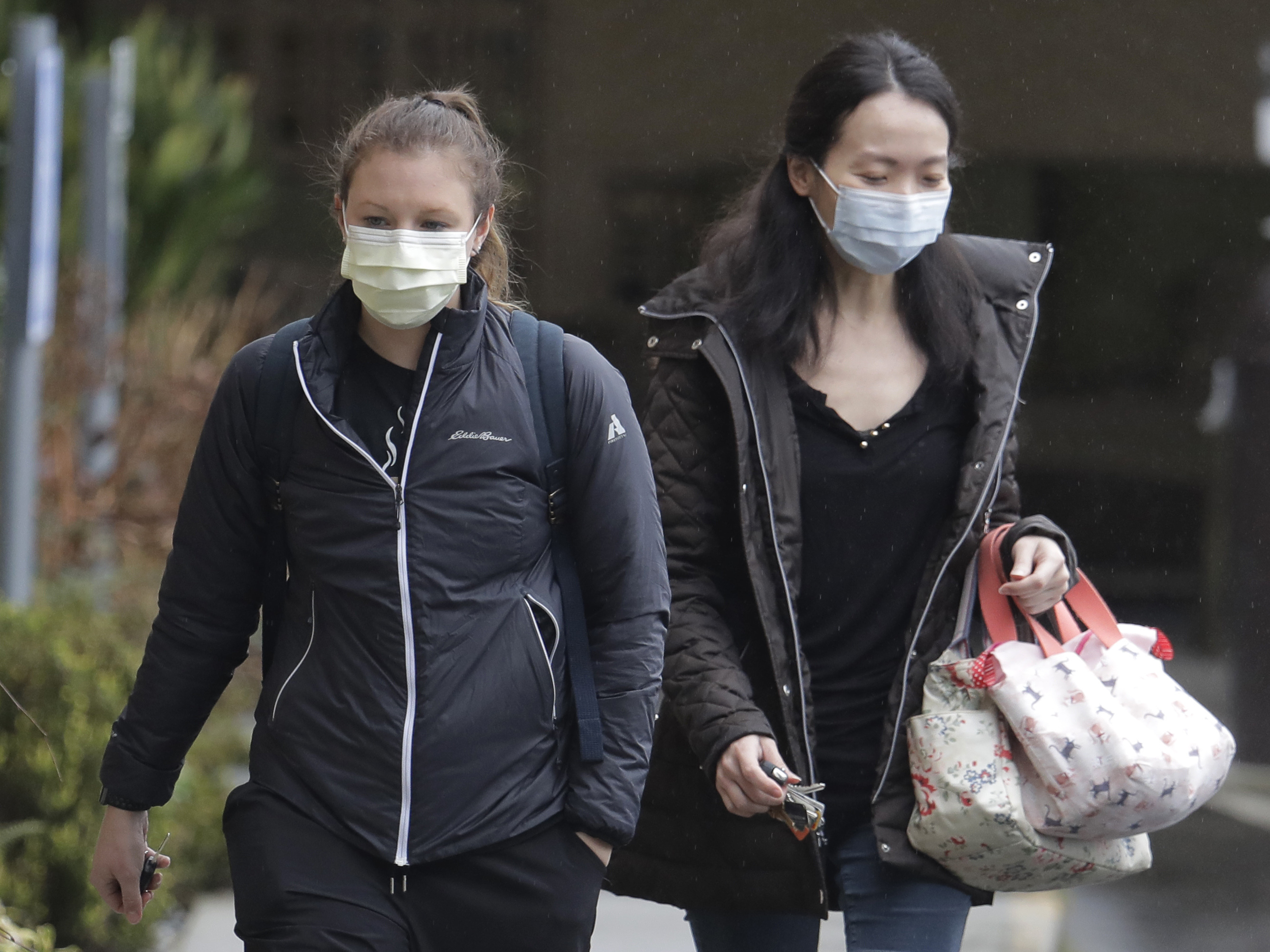 caption: Two women wearing masks walk away from the Life Care Center in Kirkland, Wash., near Seattle, where health officials are monitoring patients. An outbreak of the coronavirus is cited as the cause for two  deaths of patients who received care at the center.