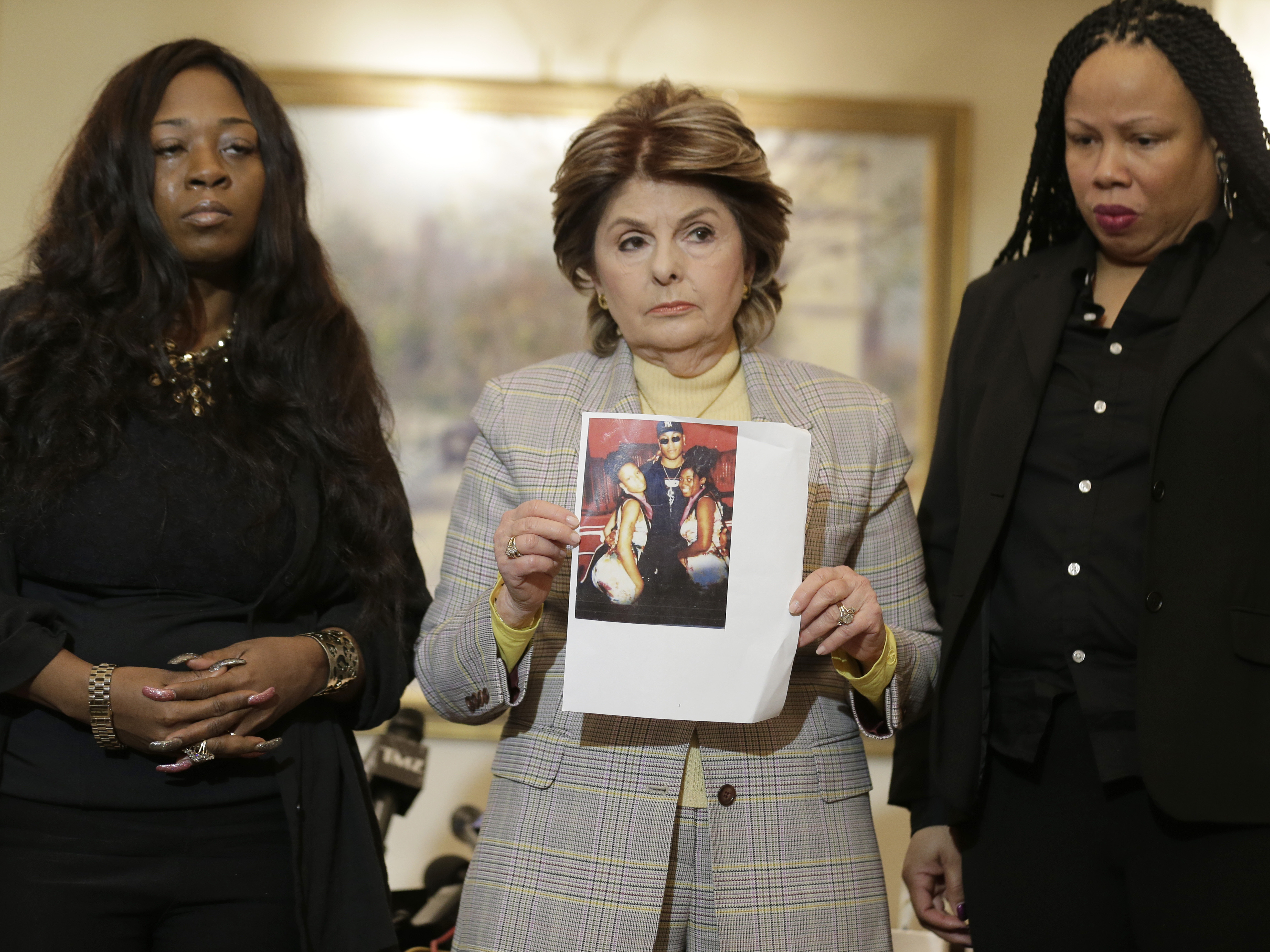 caption: Rochelle Washington (left) and Latresa Scaff (right) look on Thursday in New York City, as attorney Gloria Allred holds up a picture of them as teenagers on the night R. Kelly allegedly made sexual advances on them.