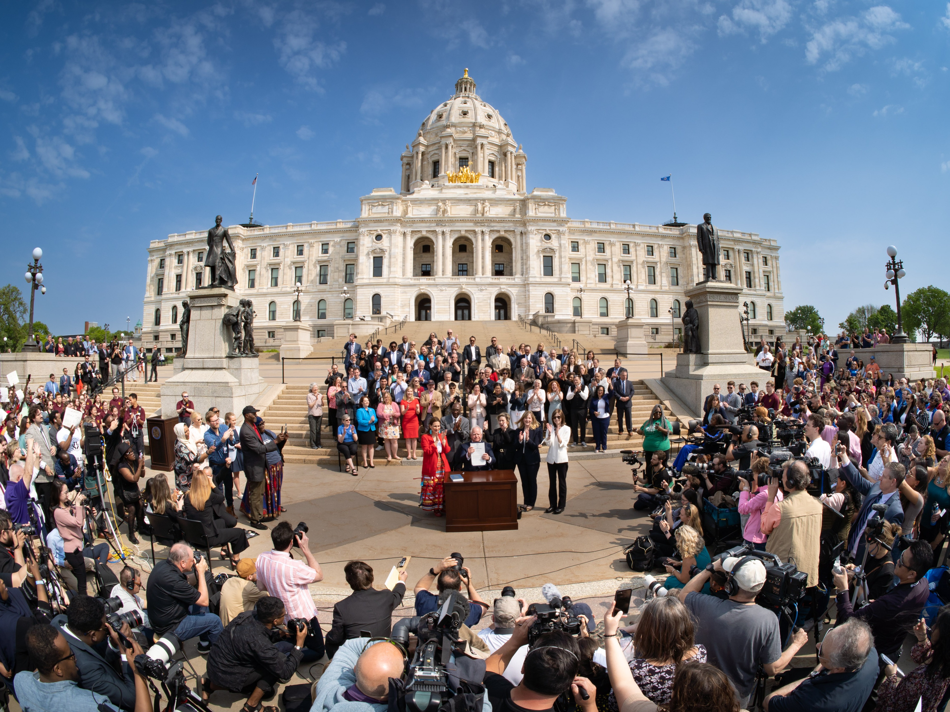 caption: Minnesota Gov. Tim Walz signs the budget bill on May 24, 2023, on the steps of the State Capitol in St. Paul, Minn., in front of hundreds of supporters.