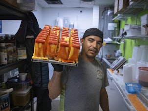caption: Manuel Vazquez, owner of Coya's artisan ice cream, poses for a photo as he carries a tray of ice pops in the kitchen of his shop in Fort Myers, Florida, U.S., February 26, 2024.