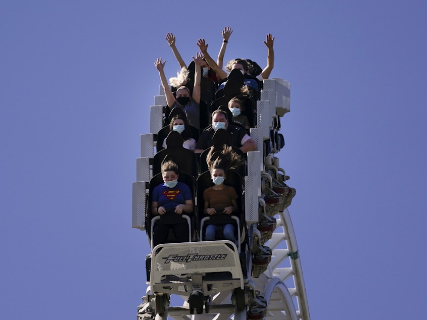 caption: Visitors wearing masks ride on a roller coaster at Six Flags Magic Mountain on its first day of reopening to members and pass holders in Valencia, Calif., on April 1, 2021.