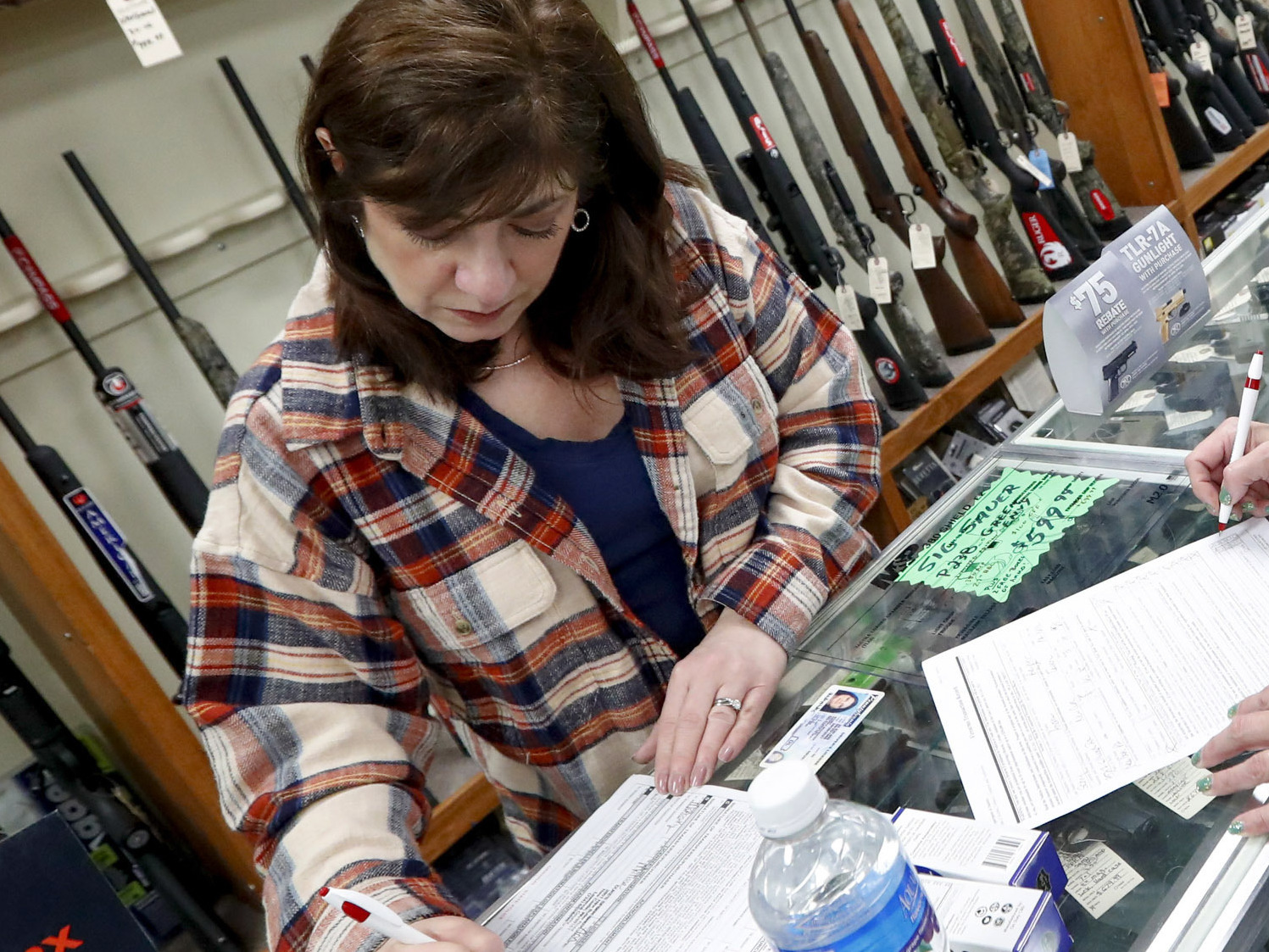 caption: Andrea Schry (right) fills out the buyer's part of legal forms to buy a handgun as shop worker Missy Morosky fills out the vendor's parts after Dukes Sport Shop in New Castle, Pa., reopened on Wednesday.