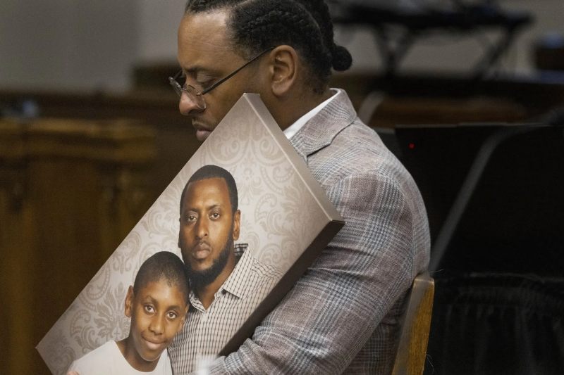 caption: Before the jury is allowed in the courtroom, Antonio Mays, Sr. holds a picture of himself and his son, Antonio Mays Jr., in Superior Court at the King County Courthouse Wednesday, Dec. 10, 2025. Before the jury arrived in the courtroom, the judge requested that he put the picture down so they wouldn’t be influenced by seeing it. 