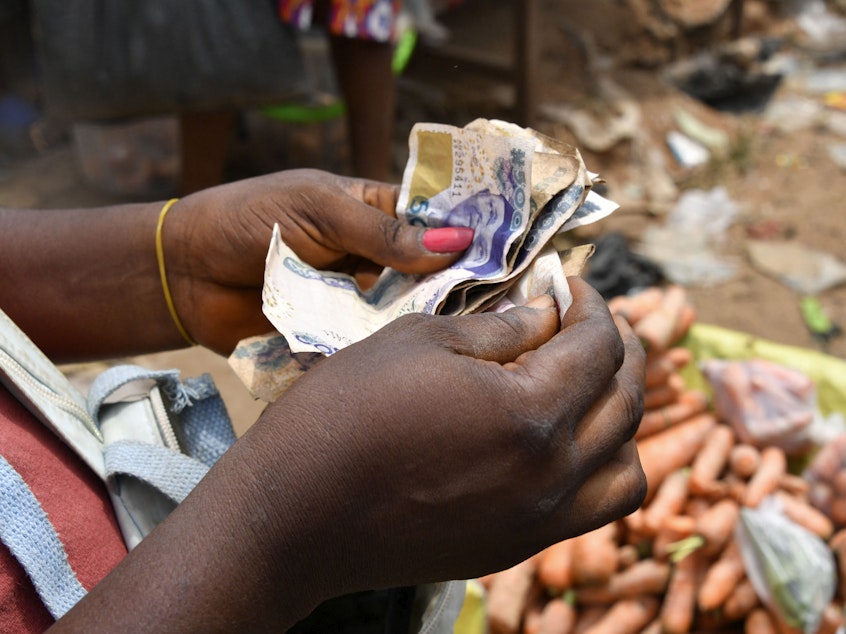 caption: A vendor in a market in Nigeria counts local bills. The country is one of dozens whose devalued currency is fueling a debt crisis.