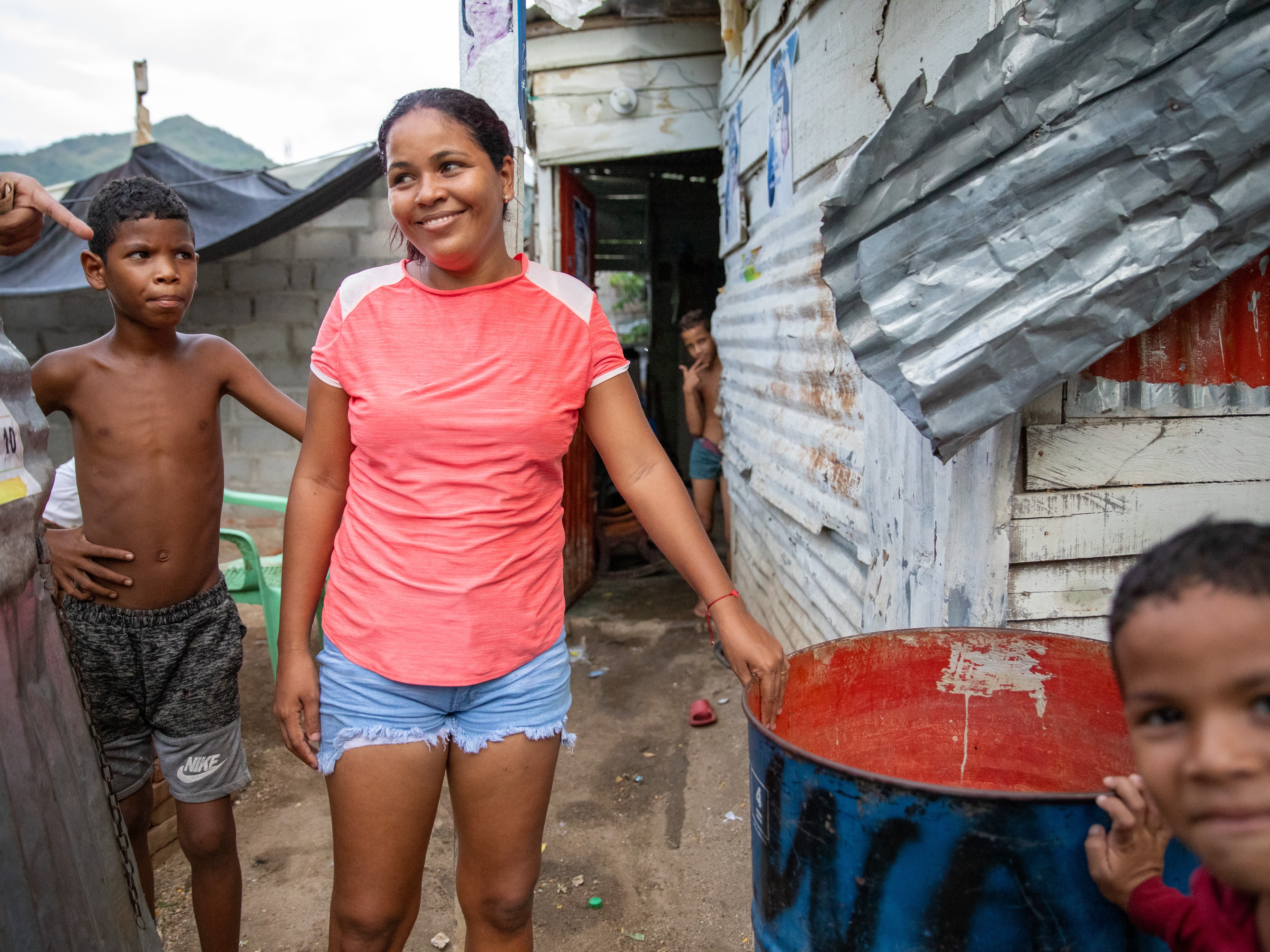 caption: In La Paz, a low-income neighborhood on the outskirts of Santa Marta, Colombia, water service from the local utility can be erratic or nonexistent. Pictured: Neighborhood kids stand next to a rain barrel positioned under a corrugated roof to collect water for household use.