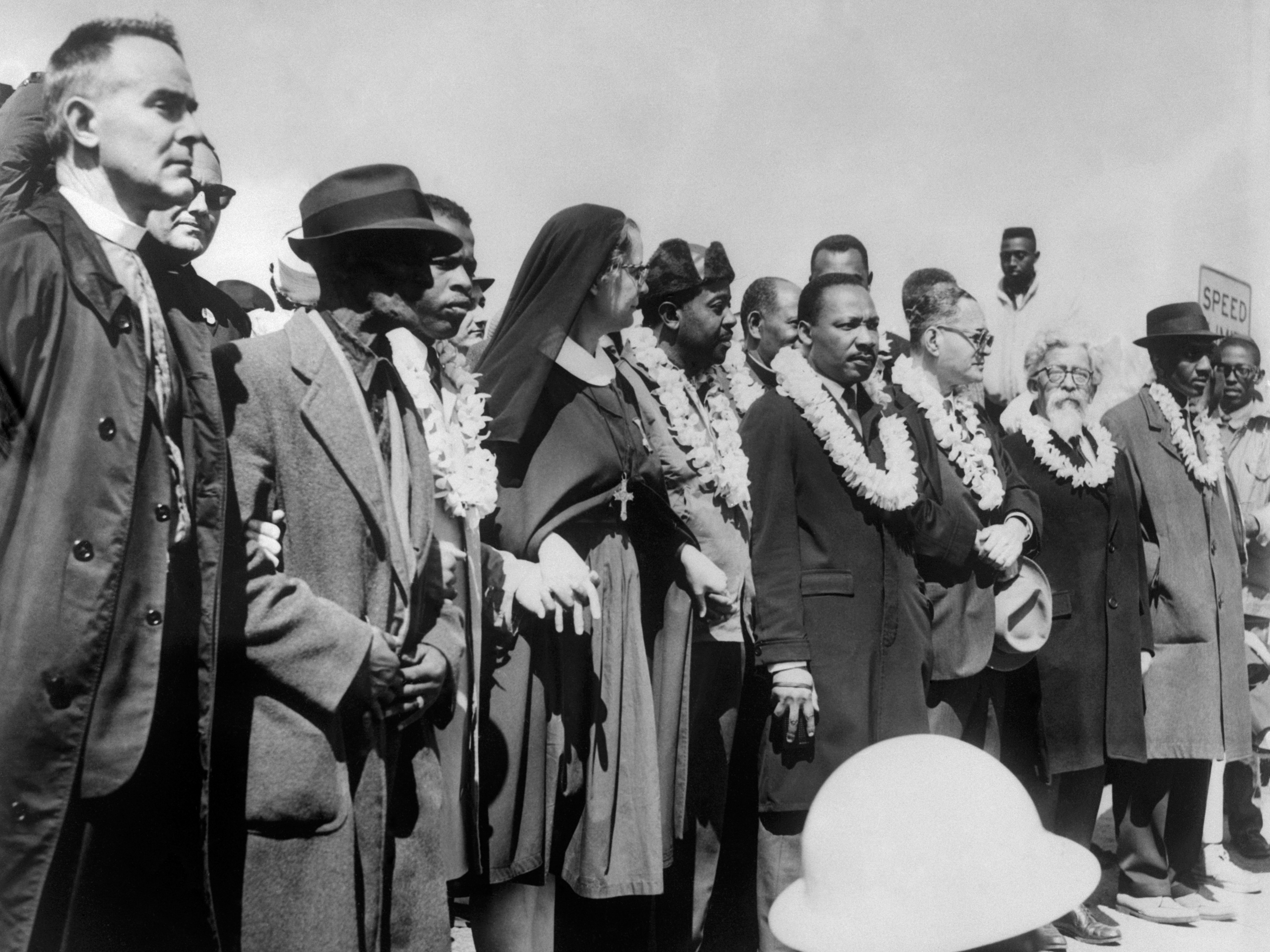 caption: Civil rights demonstrators, led by Dr. Martin Luther King (5th R), civil rights activist Ralph Abernathy (5th L), John Lewis (3rd L) and other civil and religious leaders, make their way from Selma to Montgomery on March 22, 1965 in Alabama.