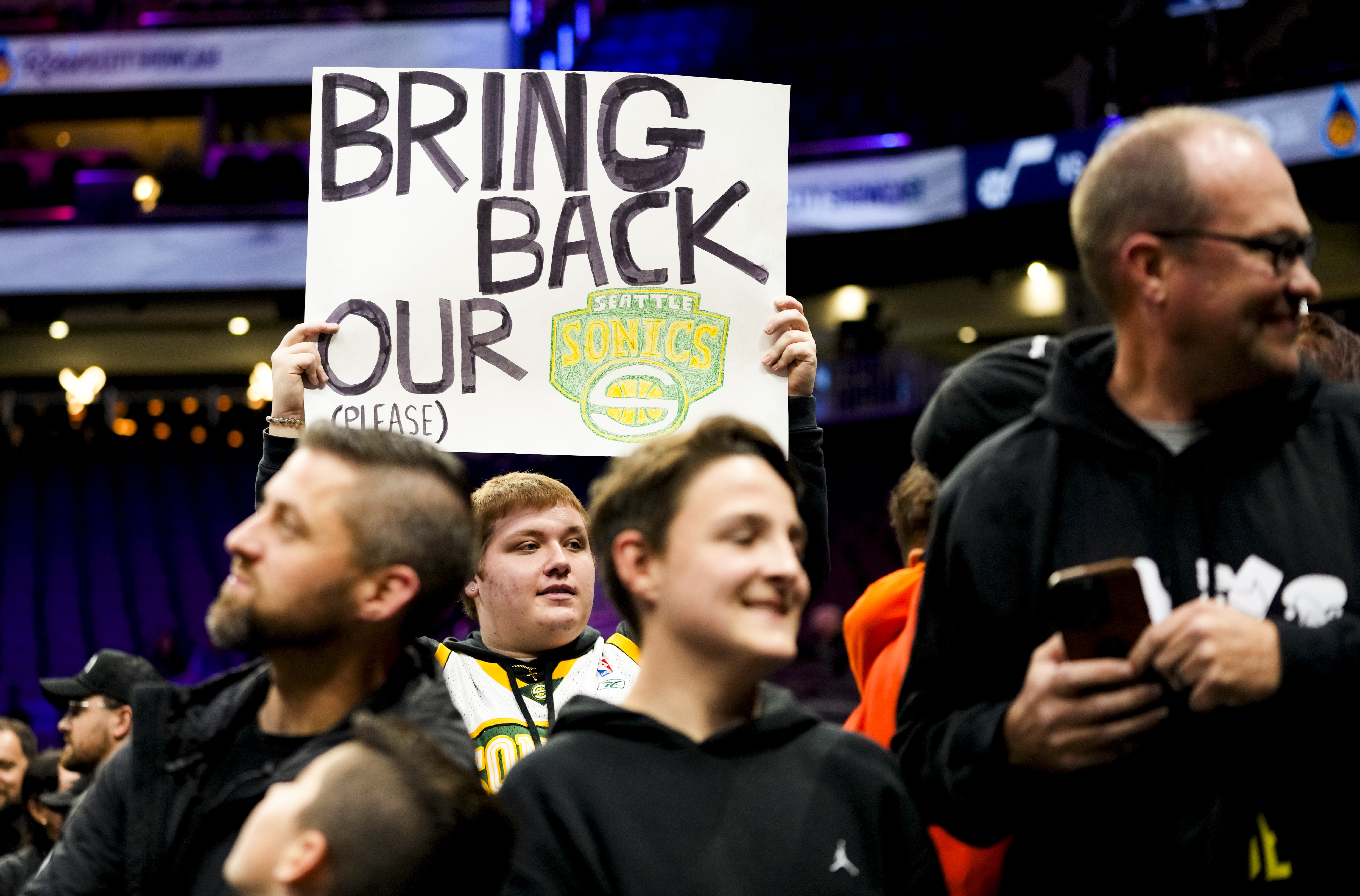 caption: A fan holds a sign asking to bring back the Seattle SuperSonics, before a preseason NBA basketball game between the Los Angeles Clippers and the Utah Jazz, Tuesday, Oct. 10, 2023, in Seattle. 