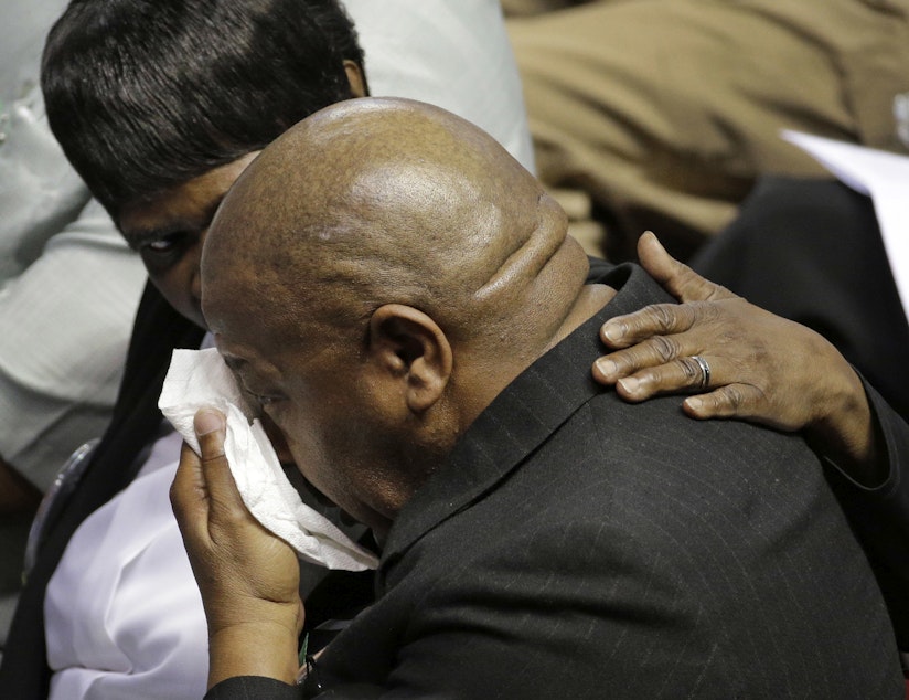 caption: A mourner is comforted during a memorial in Charleston, S.C., Friday, June 17, 2016 on the anniversary of the killing of nine black parishioners during bible study at Mother Emanuel AME Church.