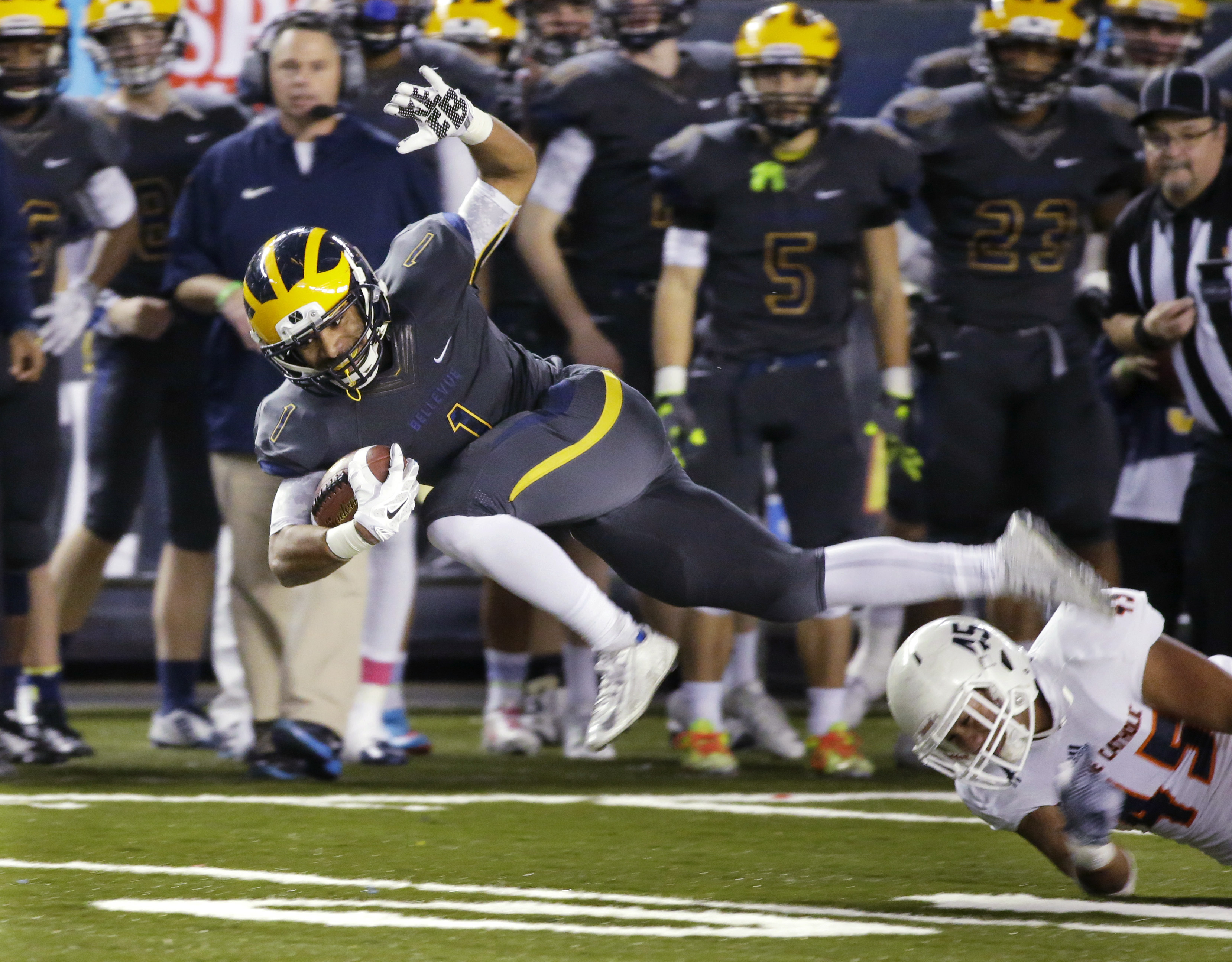 caption: Bellevue running back Isaiah Gilchrist, left, leaps to avoid a tackle attempt by Eastside Catholic's Noah Failauga during the first half of the Class 3A high school football championship Friday, Dec. 4, 2015.
