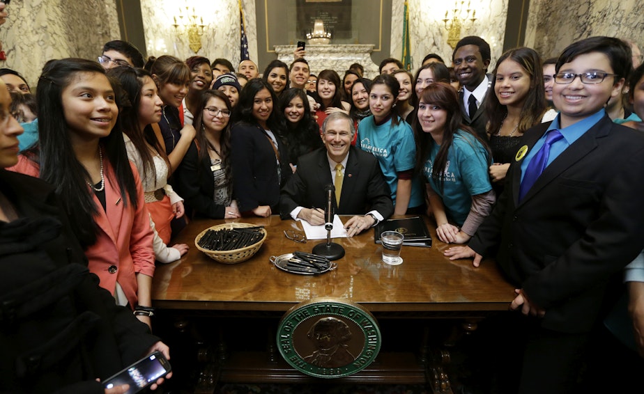caption: Washington Gov. Jay Inslee, center, poses for a photo with a group of students, after he signed into law a measure that expands state financial aid to students living illegally in the country, Wednesday, Feb. 26, 2014, at the Capitol in Olympia, Wash.