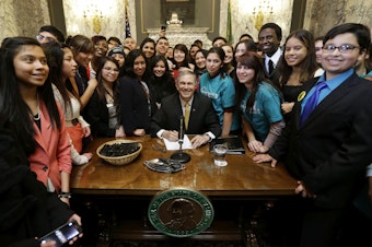 caption: Washington Gov. Jay Inslee, center, poses for a photo with a group of students, after he signed into law a measure that expands state financial aid to students living illegally in the country, Wednesday, Feb. 26, 2014, at the Capitol in Olympia, Wash.