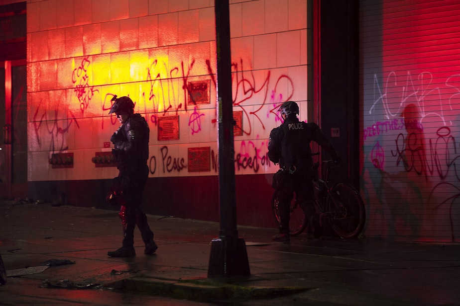 caption: Seattle police officers are shown walking near graffiti on Saturday, May 30, 2020, in Seattle. Thousands gathered in a protest following the violent police killing of George Floyd, a Black man who was killed by a white police officer who held his knee on Floyd's neck for 8 minutes and 46 seconds, as he repeatedly said, 'I can't breathe,' in Minneapolis on Memorial Day. 