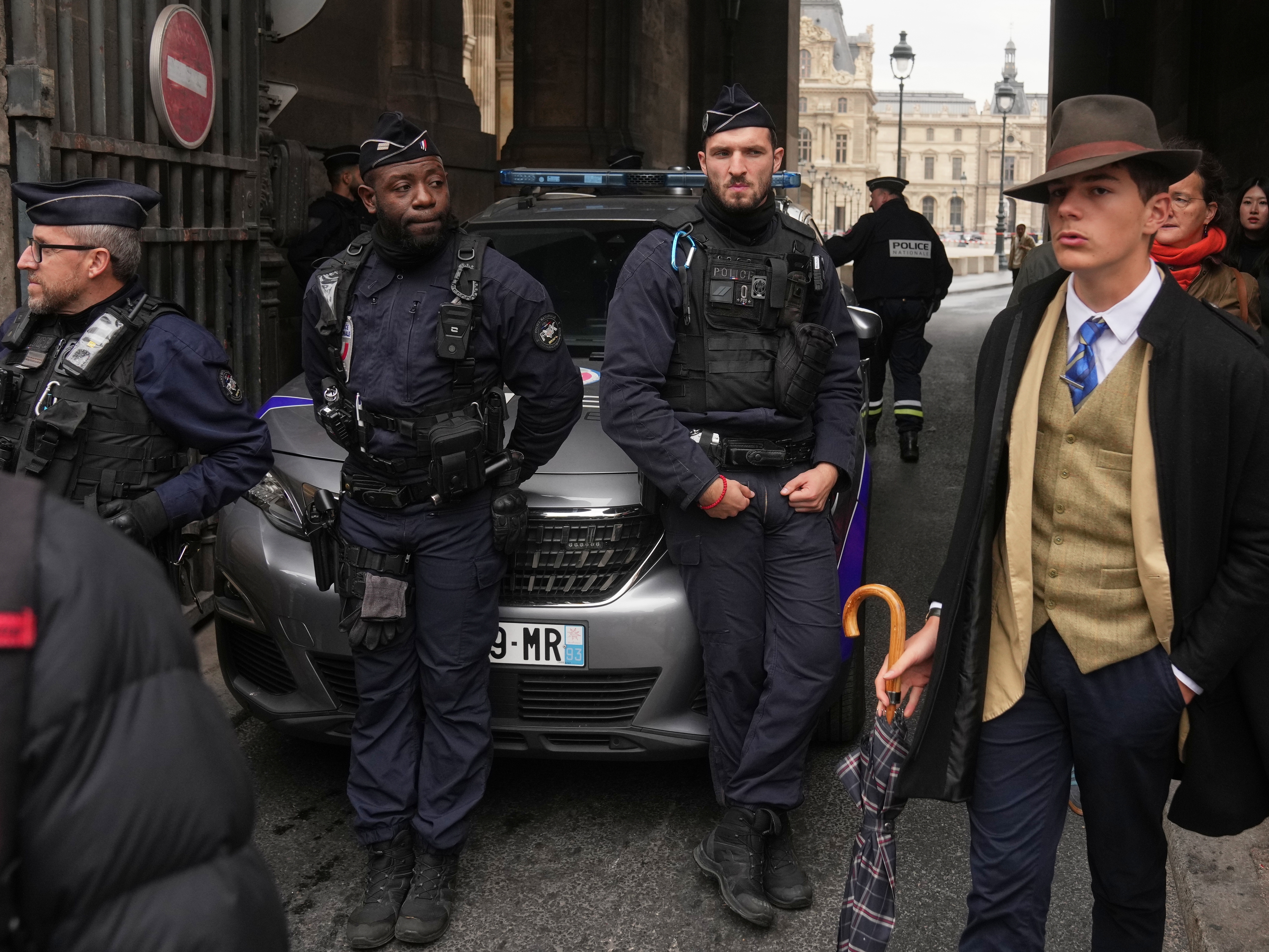caption: Pedro Elias Garzon Delvaux, right, walks past as police officers block an entrance to the Louvre after thieves carried out a daylight raid on French crown jewels, in Paris, Oct. 19, 2025.