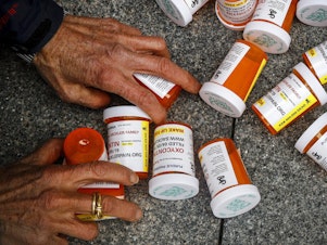 caption: A protester gathers containers that look like OxyContin bottles at an anti-opioid demonstration in front of the U.S. Department of Health and Human Services headquarters in Washington in 2019.