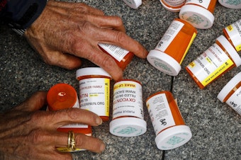 caption: A protester gathers containers that look like OxyContin bottles at an anti-opioid demonstration in front of the U.S. Department of Health and Human Services headquarters in Washington in 2019.