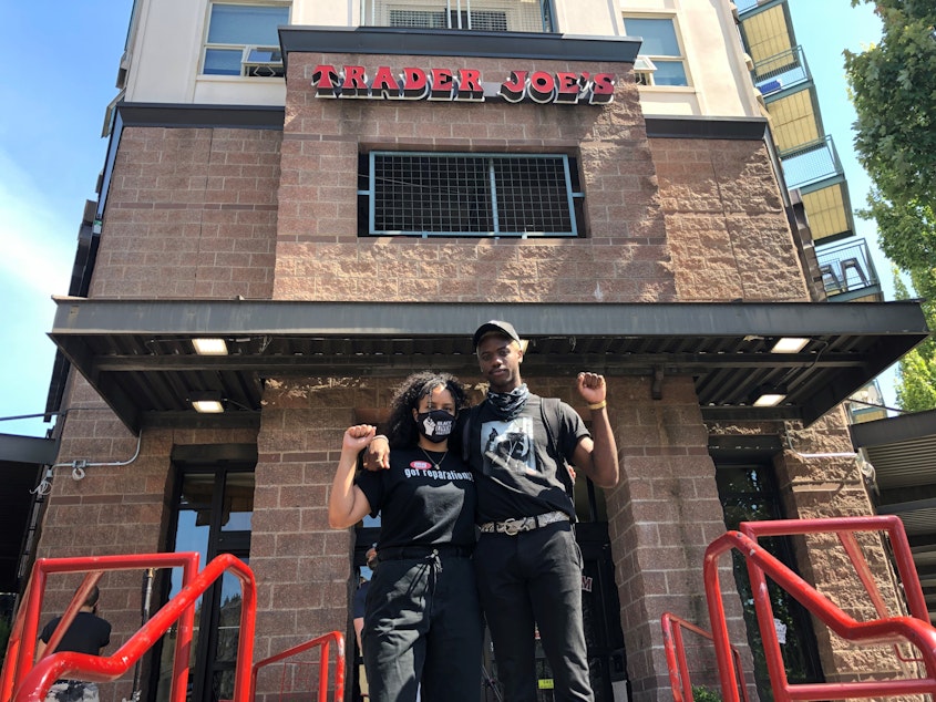 caption: Trader Joe's employees Erin Or (left) and Tre Scott (right) pose for a photo in front of the currently closed Capitol Hill store on Thursday, June 25, 2020.